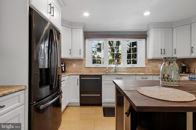 kitchen with light stone countertops, stainless steel refrigerator with ice dispenser, white cabinetry, and sink