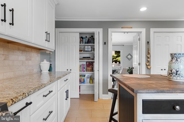 kitchen with white cabinets, decorative backsplash, crown molding, and dark stone counters