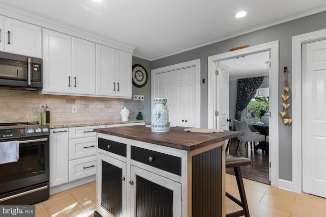 kitchen featuring butcher block countertops, backsplash, white cabinetry, and range with electric stovetop