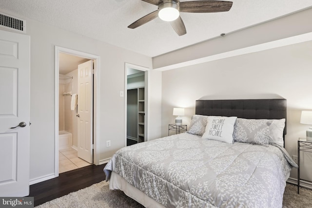 bedroom featuring hardwood / wood-style floors, a walk in closet, ensuite bath, ceiling fan, and a textured ceiling