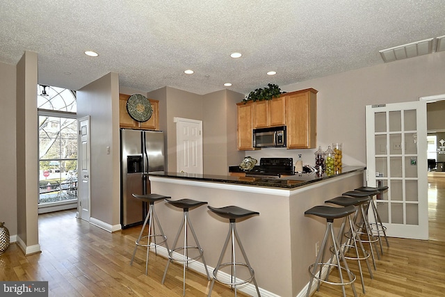 kitchen featuring stainless steel refrigerator with ice dispenser, kitchen peninsula, black range with gas cooktop, a breakfast bar area, and light wood-type flooring