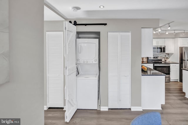 laundry room featuring hardwood / wood-style floors, a barn door, and stacked washing maching and dryer