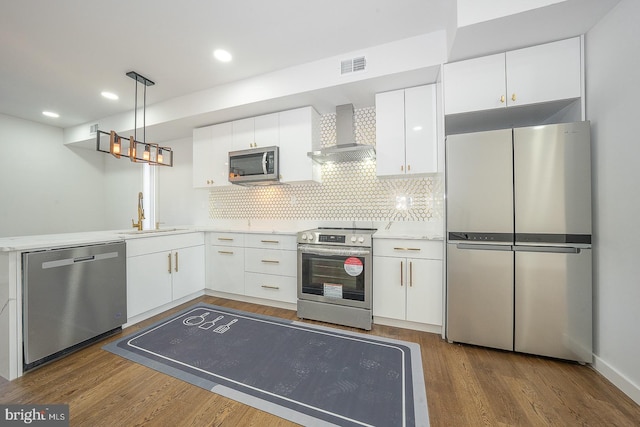 kitchen with appliances with stainless steel finishes, sink, white cabinetry, and wall chimney range hood