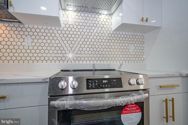 details featuring white cabinetry, wall chimney exhaust hood, light stone counters, backsplash, and stainless steel electric stove