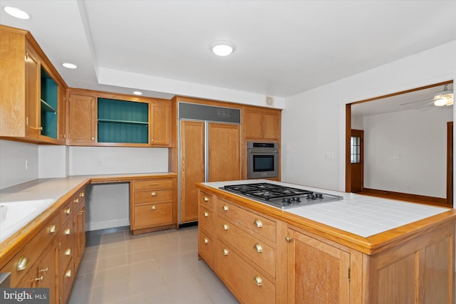 kitchen with appliances with stainless steel finishes, ceiling fan, a kitchen island, tile counters, and light tile patterned flooring