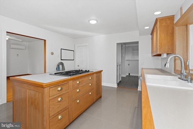 kitchen with a wall unit AC, a kitchen island, light tile patterned floors, and stainless steel gas cooktop