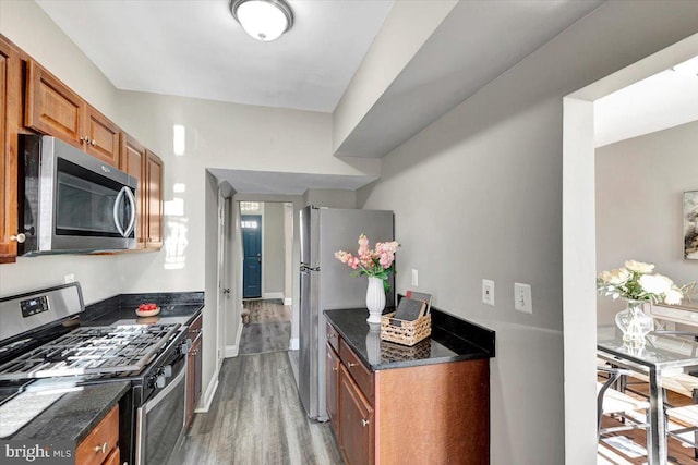 kitchen with appliances with stainless steel finishes, dark stone countertops, and hardwood / wood-style floors