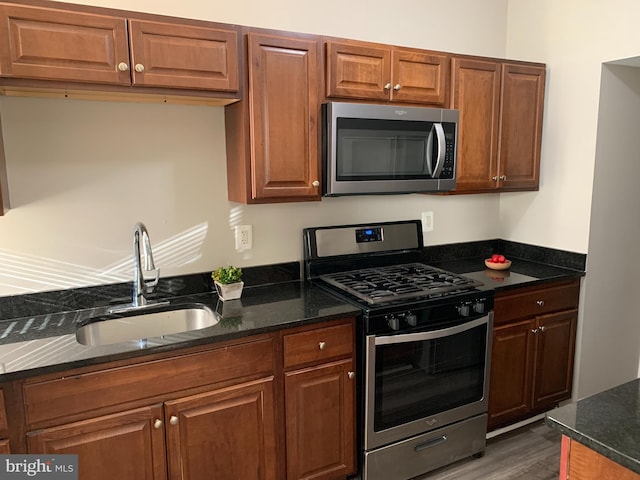 kitchen with stainless steel appliances, dark hardwood / wood-style floors, dark stone countertops, and sink