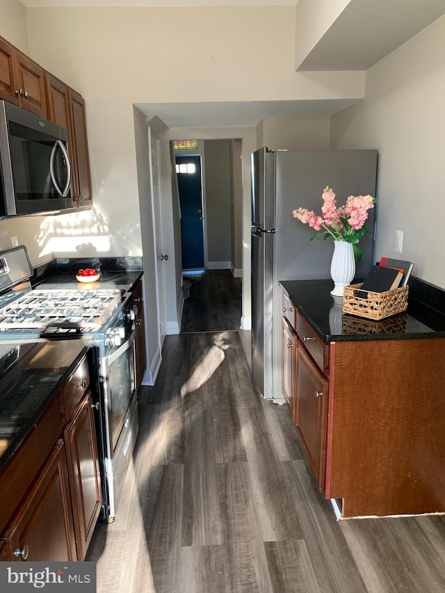 kitchen with appliances with stainless steel finishes, dark wood-type flooring, and dark stone countertops