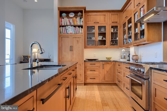 kitchen featuring dark stone counters, extractor fan, high end stainless steel range oven, sink, and light hardwood / wood-style flooring