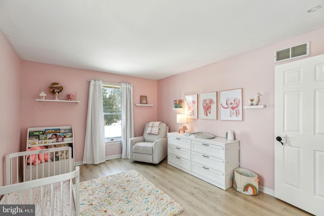 bedroom featuring light wood-type flooring and a nursery area