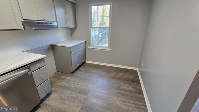 kitchen with decorative backsplash, stainless steel dishwasher, light stone counters, hardwood / wood-style flooring, and gray cabinets