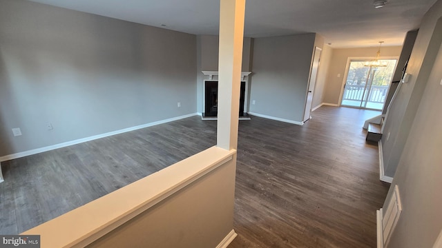 unfurnished living room featuring an inviting chandelier and dark wood-type flooring