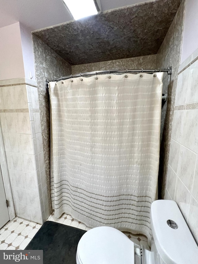 bathroom featuring a shower with shower curtain, toilet, and tile walls