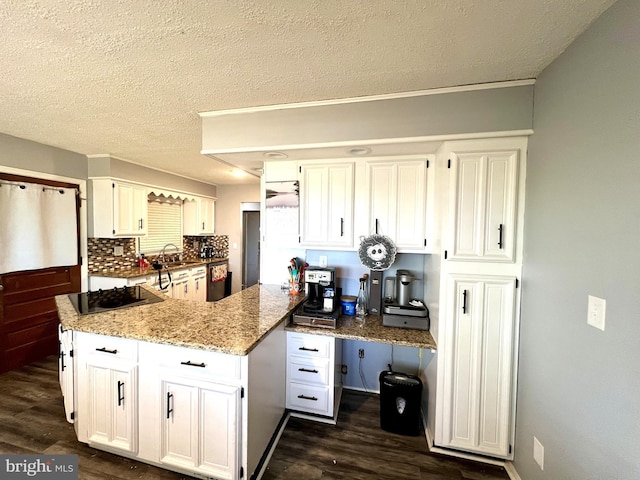 kitchen with white cabinetry, light stone countertops, backsplash, kitchen peninsula, and black stovetop