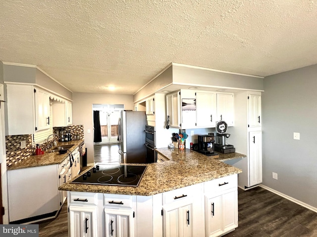 kitchen featuring light stone counters, black electric stovetop, white cabinets, and sink