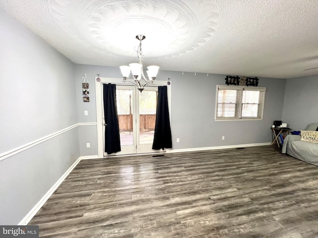 unfurnished dining area featuring dark wood-type flooring, a textured ceiling, and a chandelier