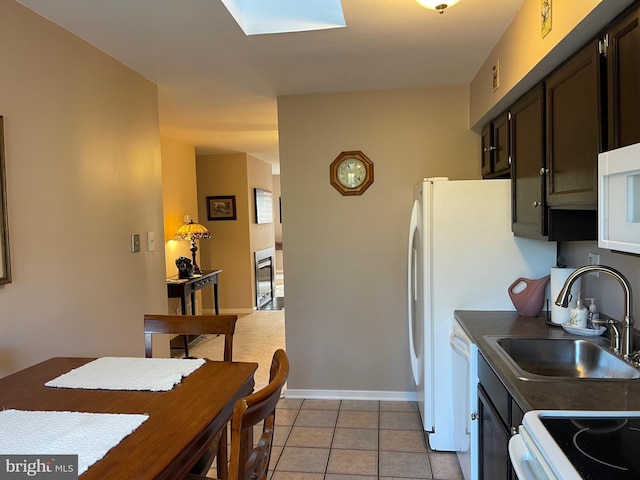 kitchen with light tile patterned flooring, white appliances, sink, and a skylight