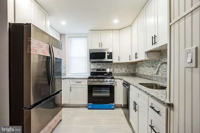 kitchen with appliances with stainless steel finishes, light stone counters, white cabinetry, and sink