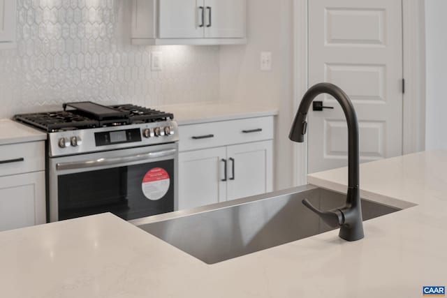 kitchen with backsplash, sink, white cabinets, and high end stainless steel range oven