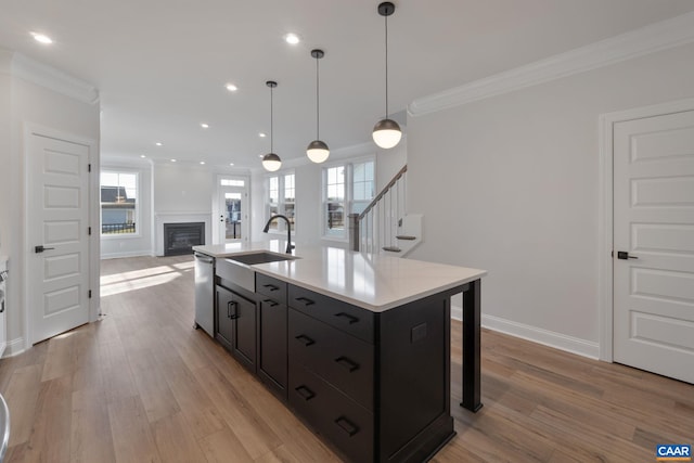 kitchen featuring stainless steel dishwasher, ornamental molding, sink, hanging light fixtures, and an island with sink