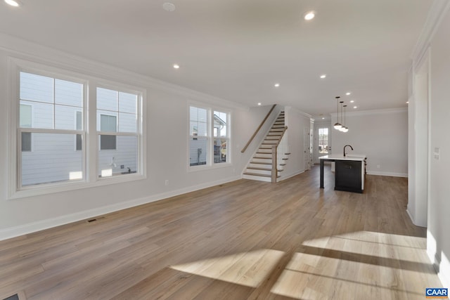 unfurnished living room with light hardwood / wood-style floors, crown molding, and sink