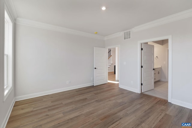 unfurnished bedroom featuring multiple windows, ensuite bathroom, wood-type flooring, and ornamental molding