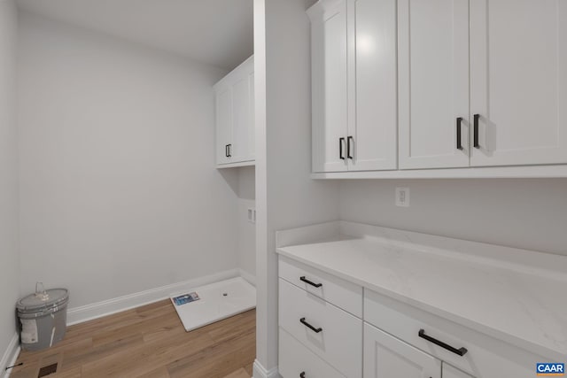 clothes washing area with cabinets and light wood-type flooring