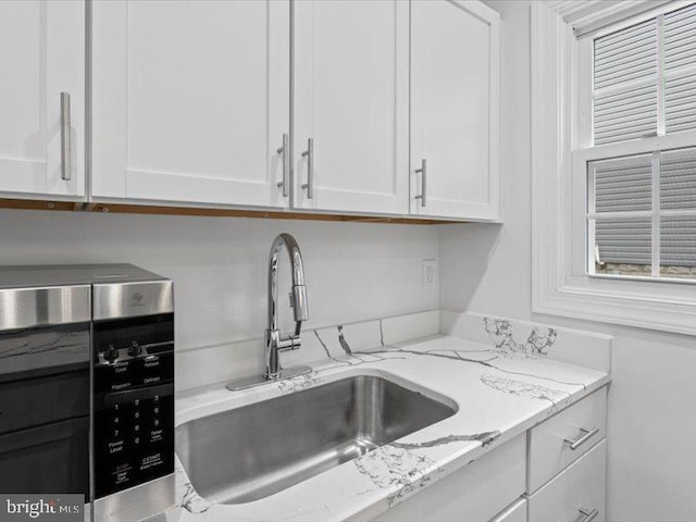 kitchen with white cabinetry, sink, and light stone countertops