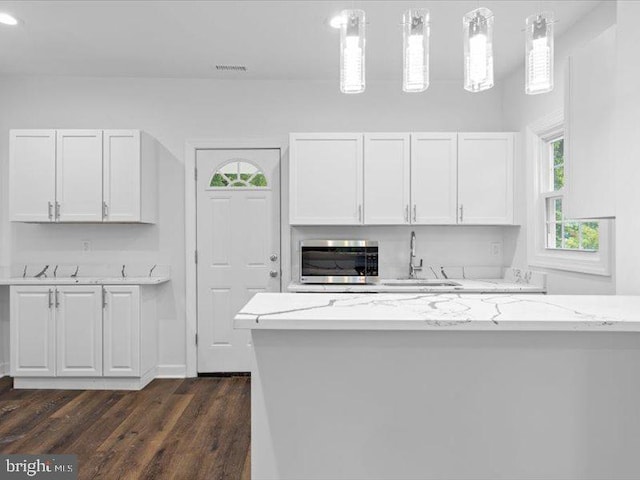 kitchen featuring white cabinetry, sink, light stone counters, dark hardwood / wood-style floors, and decorative light fixtures