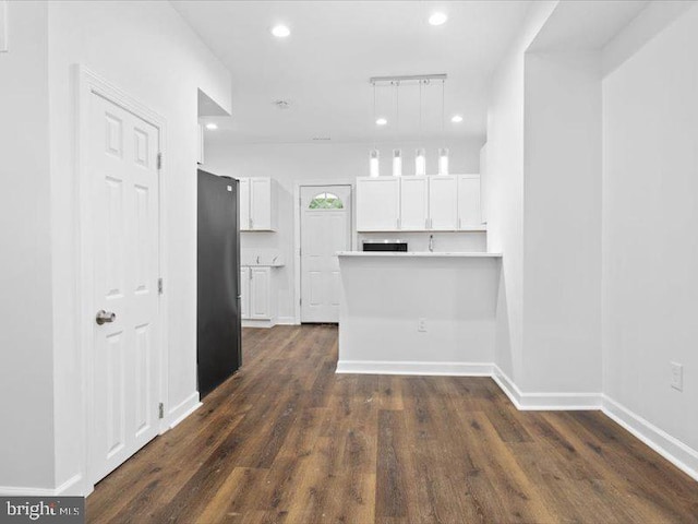 kitchen with black fridge, hanging light fixtures, kitchen peninsula, dark hardwood / wood-style floors, and white cabinetry