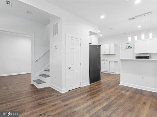 interior space featuring white cabinets, pendant lighting, black fridge, and dark wood-type flooring