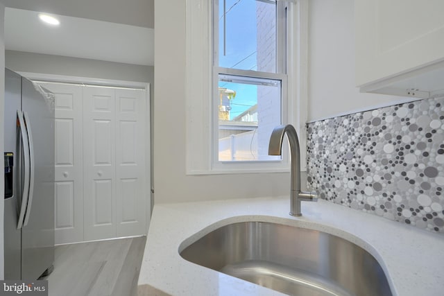 interior details featuring sink, decorative backsplash, light stone countertops, light hardwood / wood-style floors, and stainless steel fridge with ice dispenser