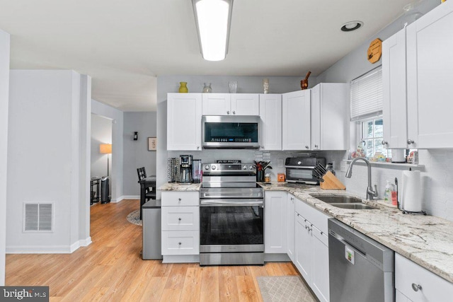 kitchen with appliances with stainless steel finishes, sink, white cabinets, light stone countertops, and light hardwood / wood-style floors