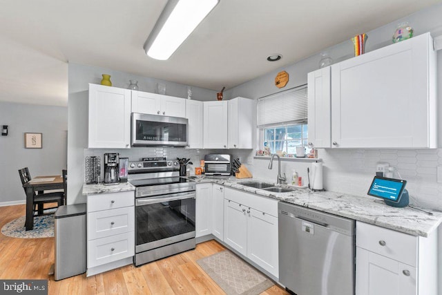 kitchen with white cabinetry, stainless steel appliances, light hardwood / wood-style floors, sink, and backsplash