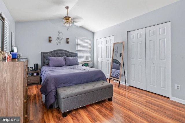 bedroom with ceiling fan, lofted ceiling, hardwood / wood-style flooring, and two closets