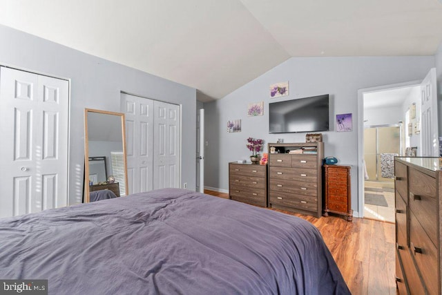 bedroom with multiple closets, light wood-type flooring, vaulted ceiling, and ensuite bath