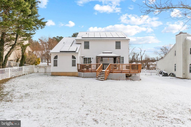 snow covered back of property with a wooden deck, a gazebo, and solar panels