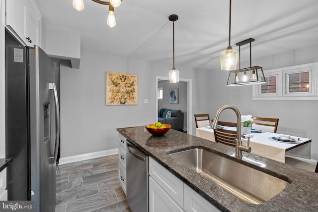 kitchen featuring sink, stainless steel appliances, dark stone countertops, pendant lighting, and white cabinets