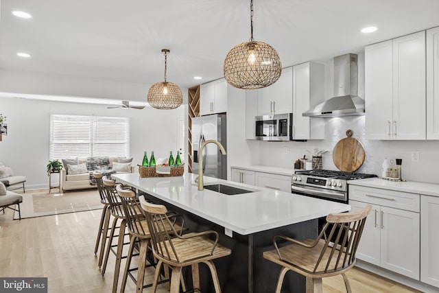 kitchen with white cabinetry, wall chimney exhaust hood, stainless steel appliances, pendant lighting, and a breakfast bar