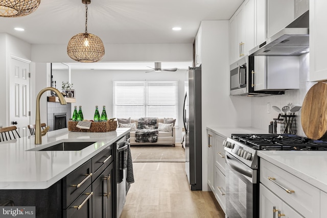 kitchen featuring ceiling fan, sink, wall chimney range hood, white cabinets, and appliances with stainless steel finishes