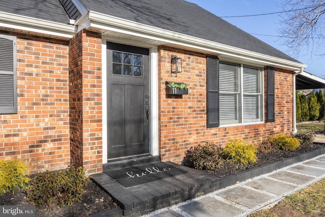 property entrance with a shingled roof and brick siding