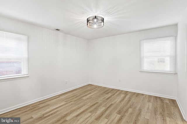 empty room featuring baseboards, visible vents, and light wood finished floors