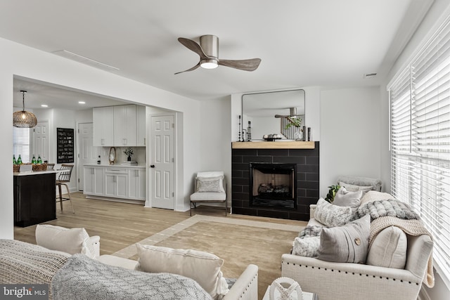 living area with light wood finished floors, visible vents, a ceiling fan, a tiled fireplace, and recessed lighting