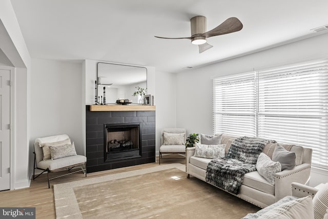 living room featuring a ceiling fan, visible vents, a tiled fireplace, and wood finished floors