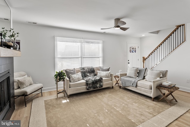 living room featuring ceiling fan, light wood-type flooring, and a tile fireplace