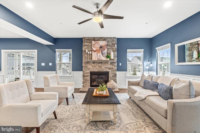 living room featuring light wood-type flooring, ceiling fan, a wealth of natural light, and a fireplace