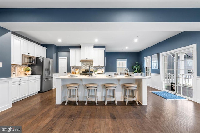 kitchen featuring white cabinetry, a breakfast bar area, stainless steel appliances, a kitchen island with sink, and dark wood-type flooring