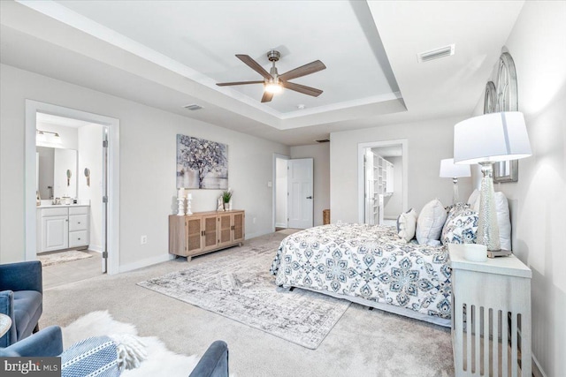 carpeted bedroom featuring ensuite bath, ceiling fan, and a tray ceiling