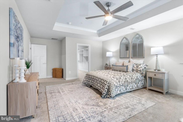 bedroom with a spacious closet, a closet, a raised ceiling, carpet flooring, and ceiling fan